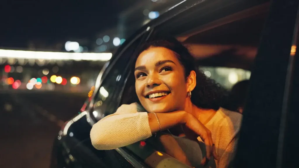 Woman smiling during a late night road trip with city lights in the background